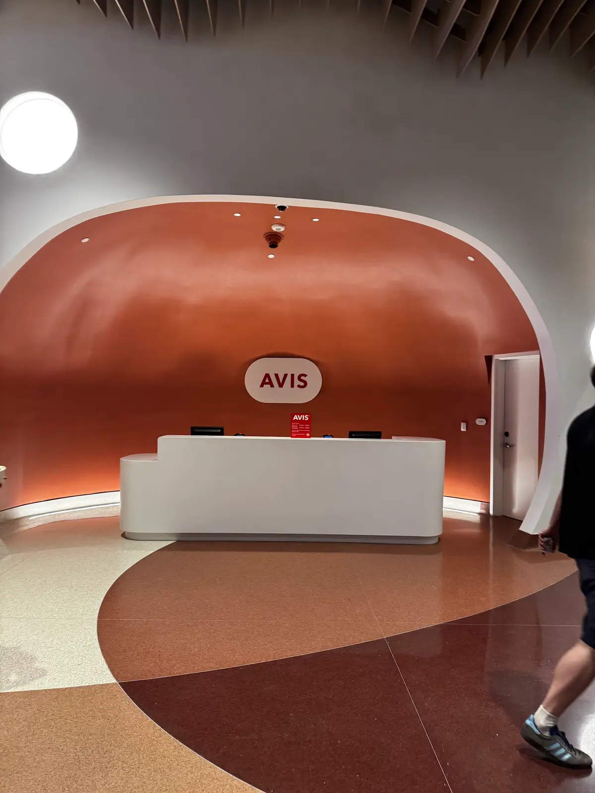 Balcão da locadora Avis em Orlando, com parede curva em tom terracota e o logotipo da empresa