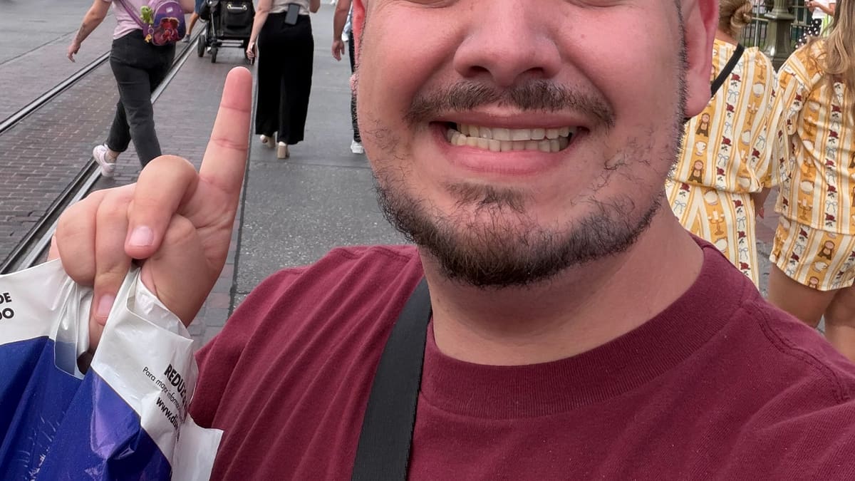 Thomaz, guia da Desenrola, sorri em selfie apontando para o castelo ao fundo, na Disneyland (Califórnia)