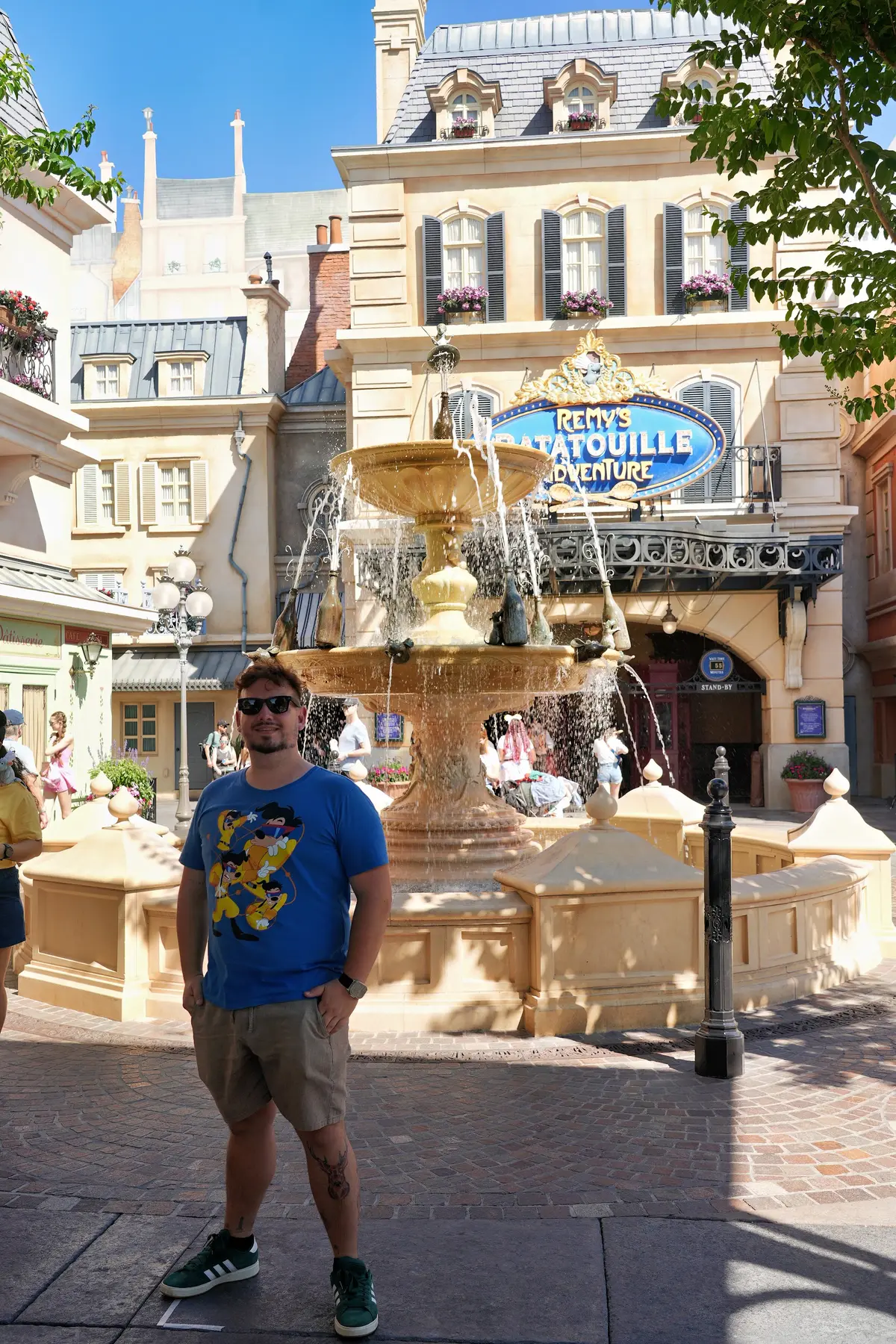 Thomaz na fonte do pavilhão da França, com a entrada do Remy's Ratatouille Adventure ao fundo, no EPCOT