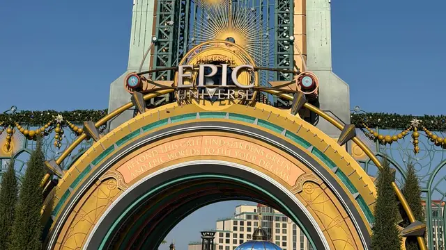 Portal de entrada do Epic Universe, com a torre Chronos e o arco dourado sob céu azul, na Universal Orlando