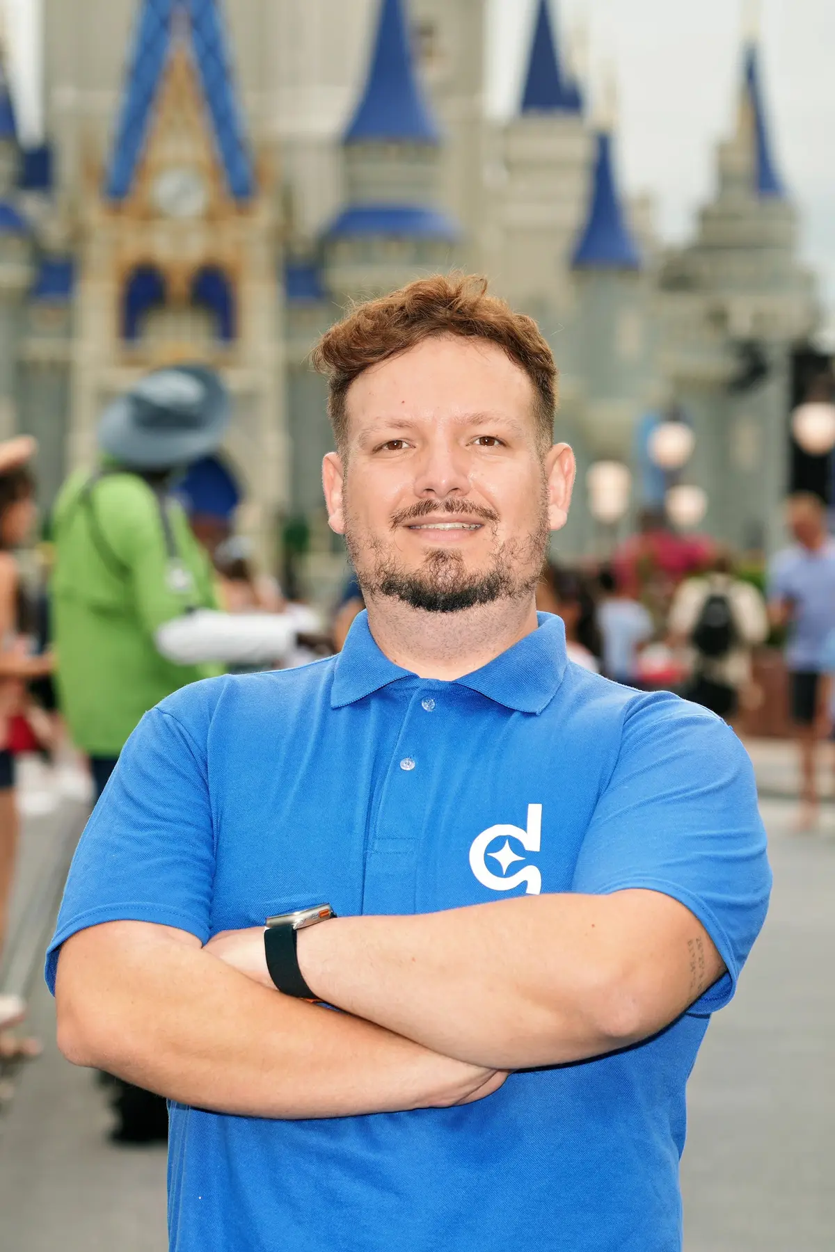 Thomaz, ex-cast member e guia da Desenrola, de polo azul e braços cruzados diante do castelo do Magic Kingdom