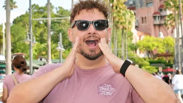 Thomaz, guia da Desenrola, com as mãos na boca como quem chama o grupo, diante da Tower of Terror