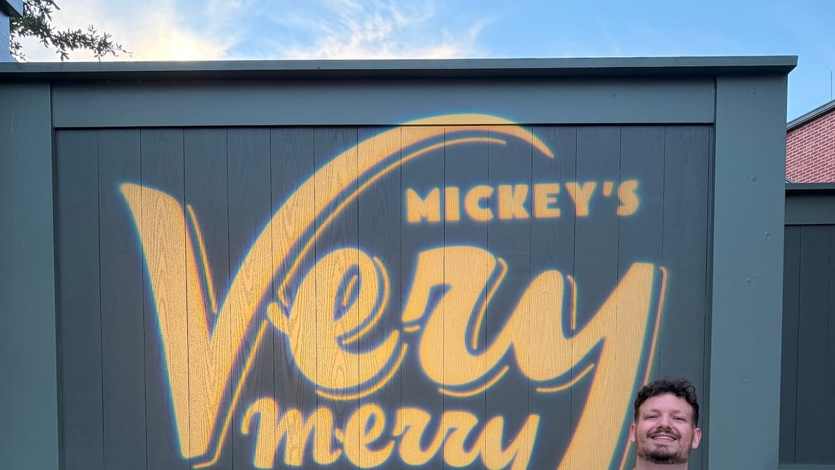 Thomaz faz joinha diante do painel da Mickey's Very Merry Christmas Party, a festa de Natal do Magic Kingdom