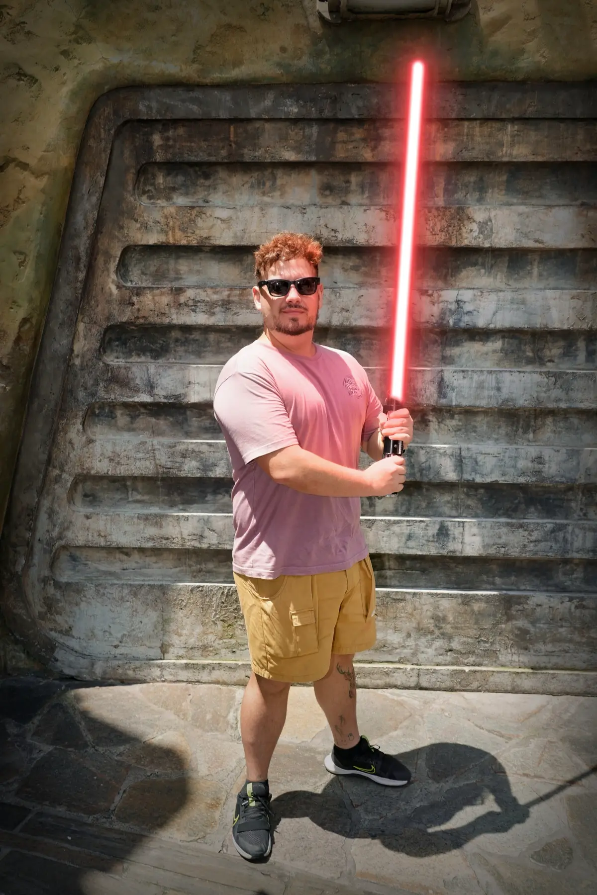 Thomaz com sabre de luz vermelho diante de uma parede de pedra de Batuu, em Galaxy's Edge, no Hollywood Studios