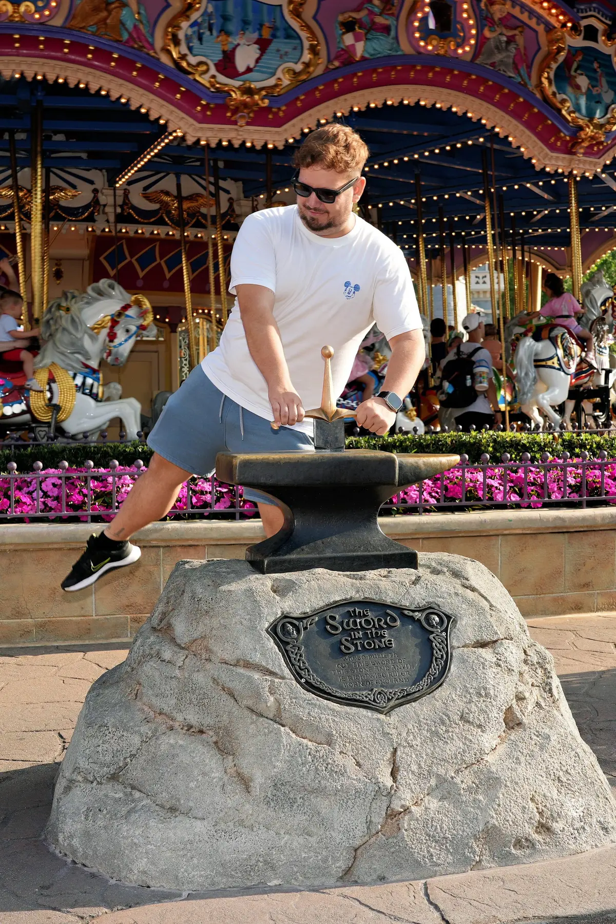 Thomaz finge tirar a espada da pedra diante do carrossel do Príncipe Encantado, na Fantasyland do Magic Kingdom