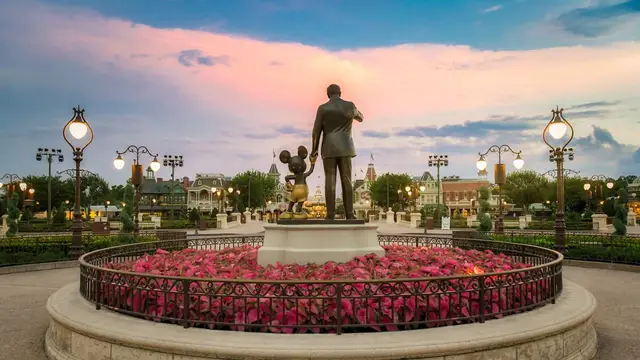 Estátua Partners, de Walt Disney e Mickey, com canteiro de flores e céu rosado ao entardecer no Magic Kingdom