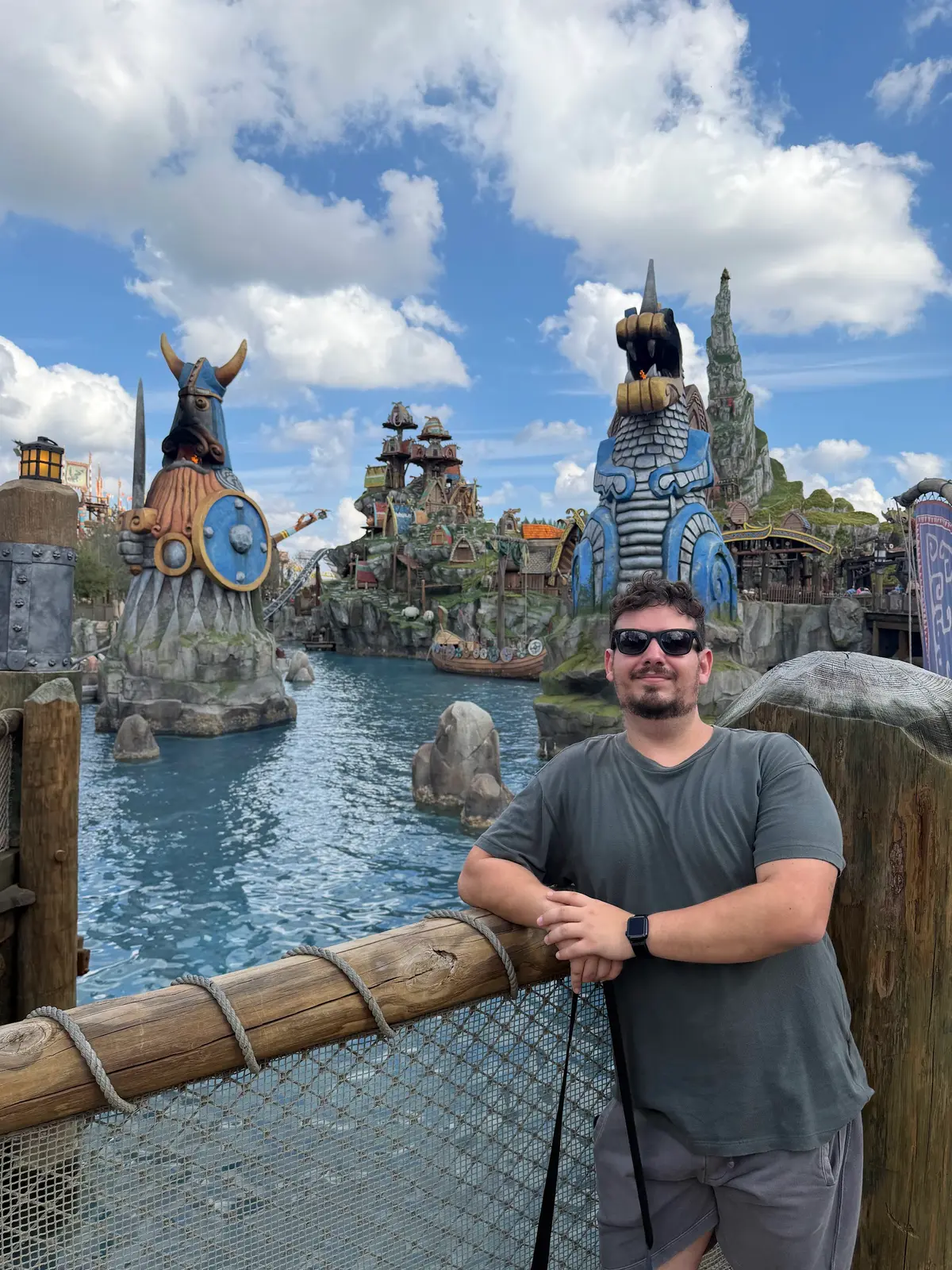 Thomaz apoiado na cerca da lagoa da Isle of Berk, com estátuas vikings ao fundo, no Epic Universe da Universal Orlando