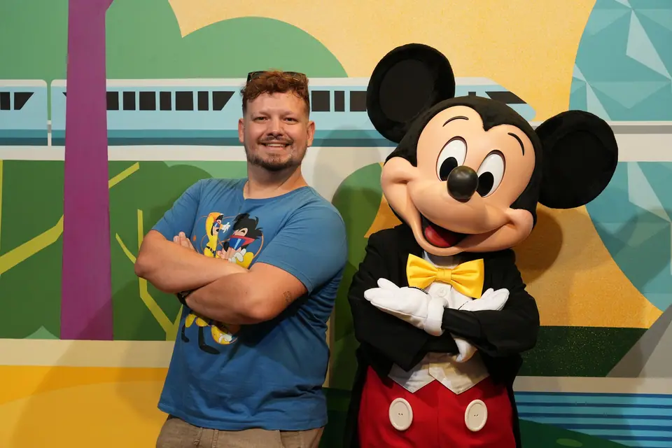Thomaz de braços cruzados ao lado do Mickey, que imita a pose, no encontro com personagens do EPCOT