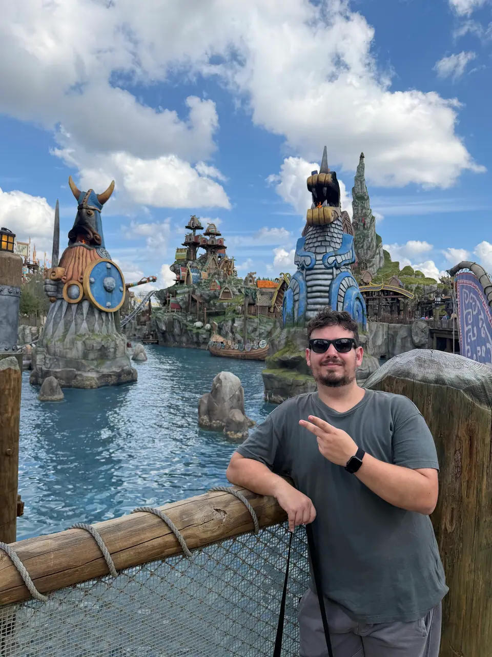 Thomaz em pose divertida apontando para a câmera na Isle of Berk, lagoa e estátuas vikings ao fundo
